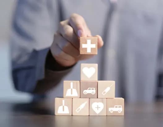 Person stacking wooden blocks with healthcare and insurance icons, symbolizing health protection and medical services.
