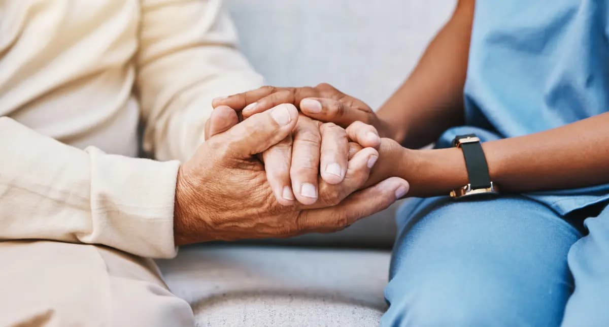 Healthcare worker holding patient's hands in supportive clinical interaction.